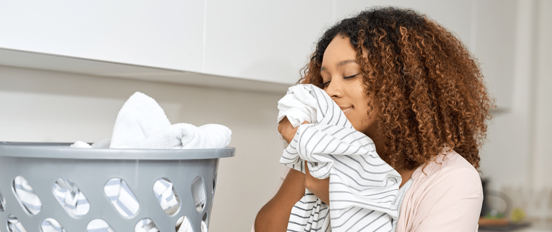 Woman enjoying the fresh scent of clean laundry in the laundry room with a basket of freshly washed clothes nearby.