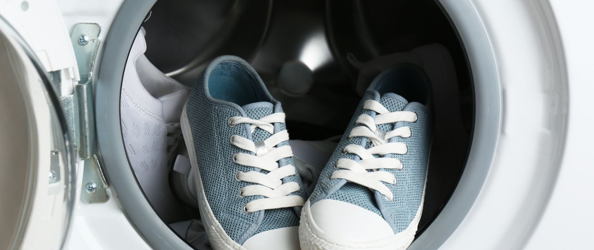 Blue and white sneakers inside a washing machine, ready for cleaning.