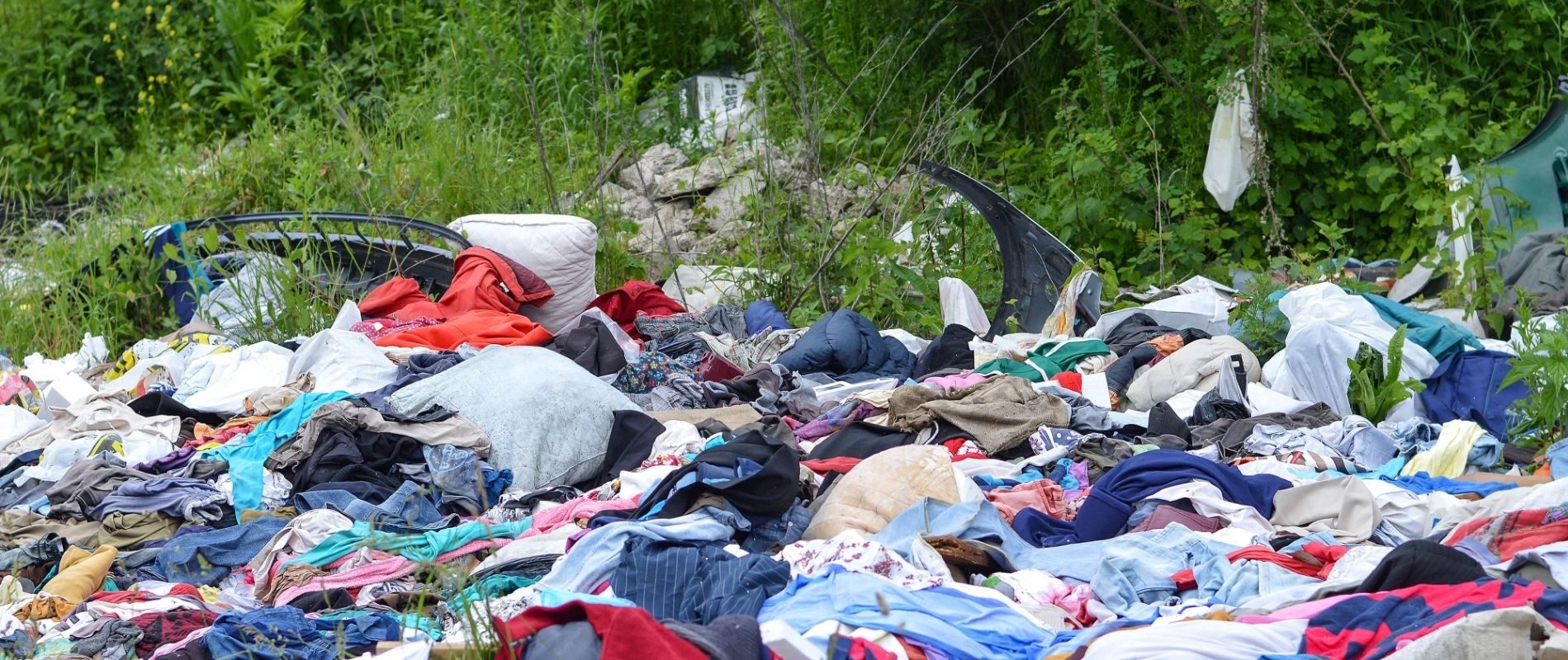 Piles of unwanted clothes and textiles dumped in a neglected outdoor area, highlighting the environmental impact of waste.