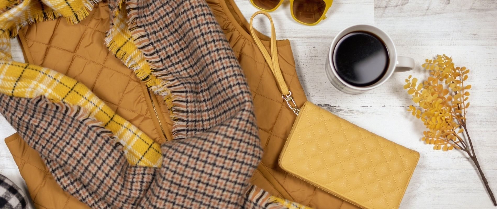 Fashionable yellow and brown winter accessories with coffee and fall decor on a wooden background. Trendy autumn vibes.