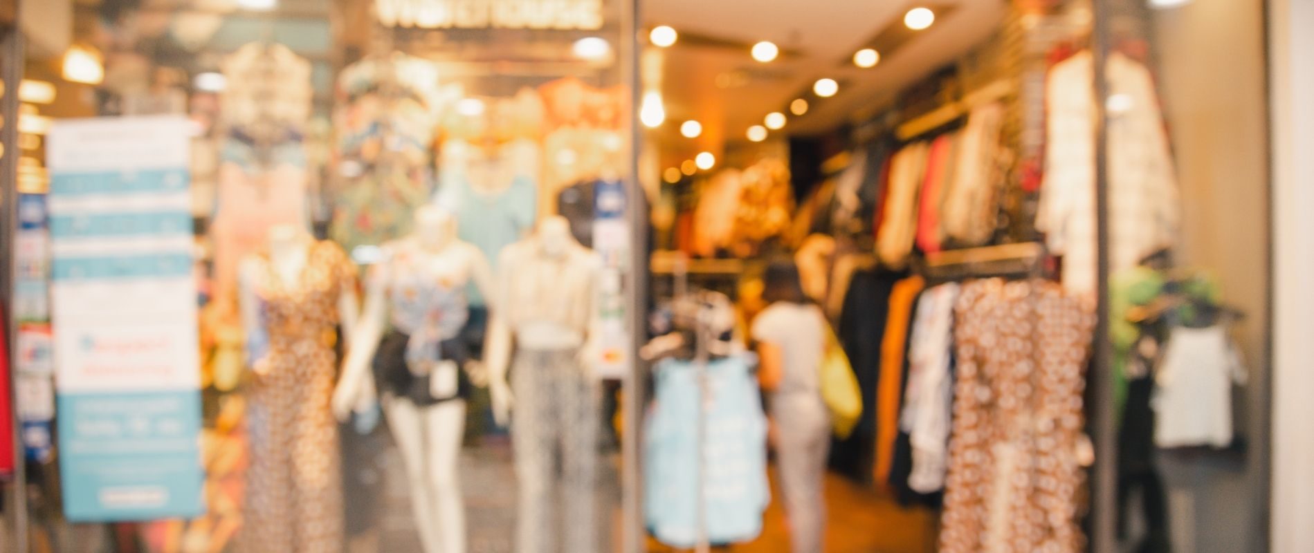 Blurred image of a vibrant clothing store with mannequins displaying trendy outfits in the front window.