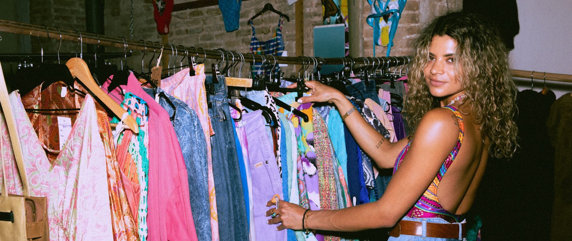 Woman browsing colorful vintage clothes in a boutique, wearing a patterned top, with a smile.