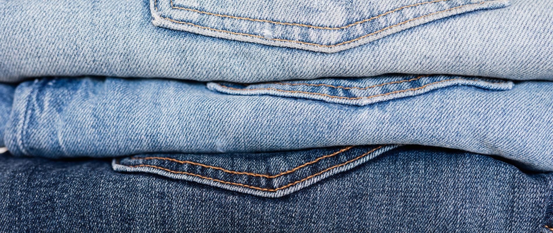 Stack of folded blue denim jeans with back pockets visible. Various shades, top view. Perfect for casual wear.