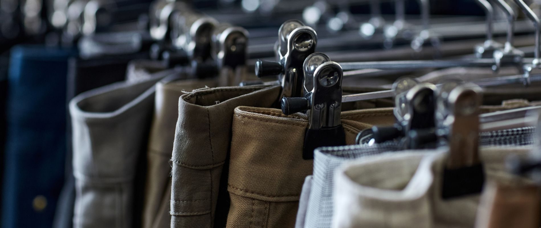 Close-up of various pants hanging on a clothes rack with metal hangers in a store.