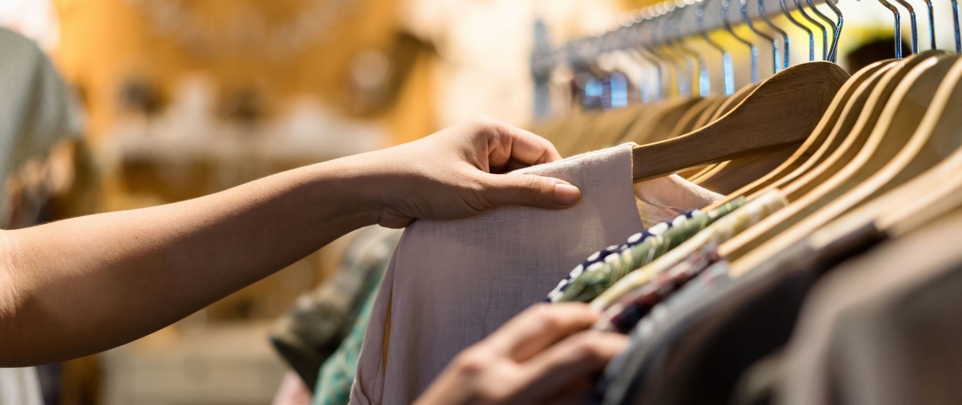 Shopping for clothes in a store, a person browses garments on hangers. Retail therapy and fashion choices.