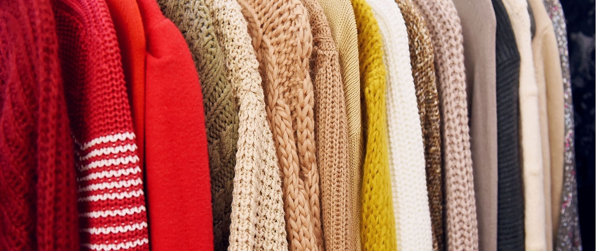 Colorful knit and wool sweaters hanging in a row on a clothing rack. Cozy winter fashion.