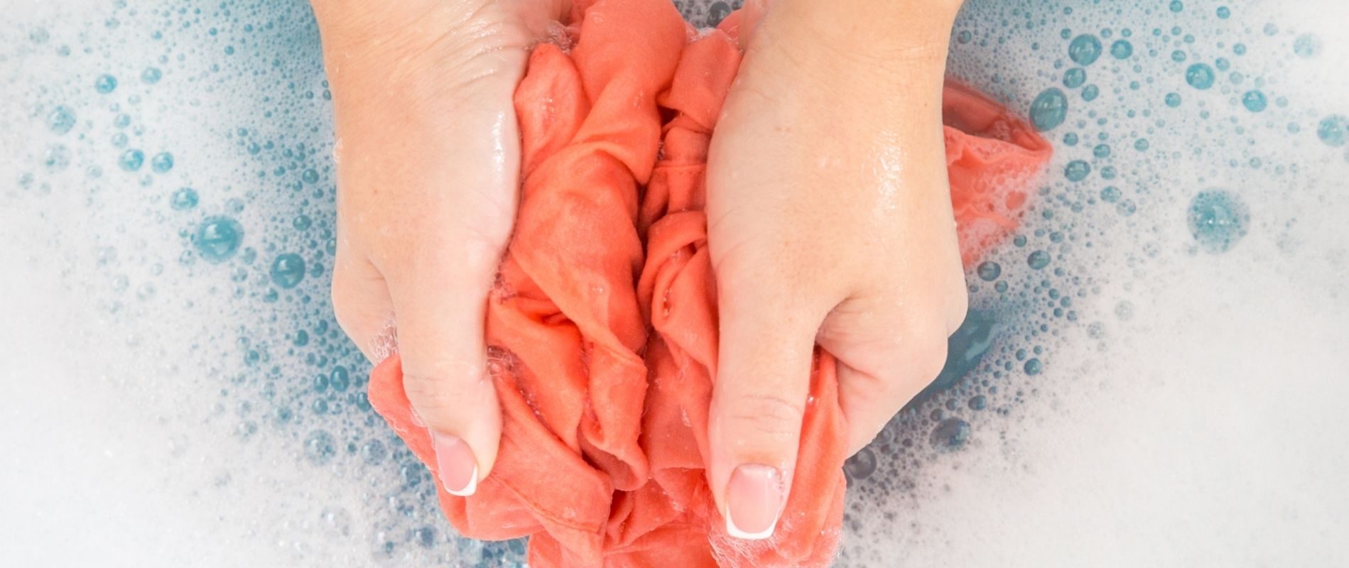 Hands washing a red garment in soapy water, close-up. Handwashing delicate clothes, laundry care.