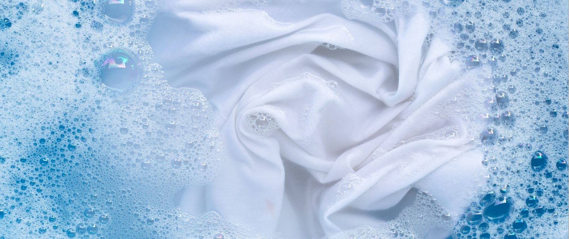 White fabric in soapy water with bubbles, demonstrating effective laundry cleaning. Clean clothes, fresh wash.