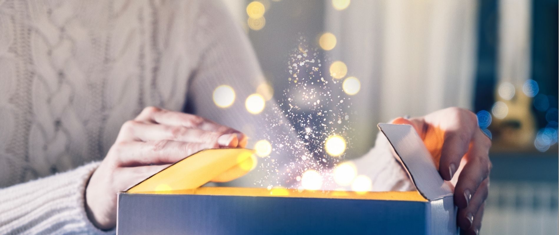 Person opening a magical gift box with glowing sparkles and bokeh lights, creating a festive, enchanting atmosphere.