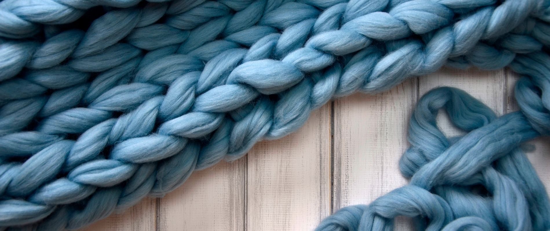 Close-up of chunky blue knitted blanket on white wooden surface. Cozy home decor, soft and warm material.