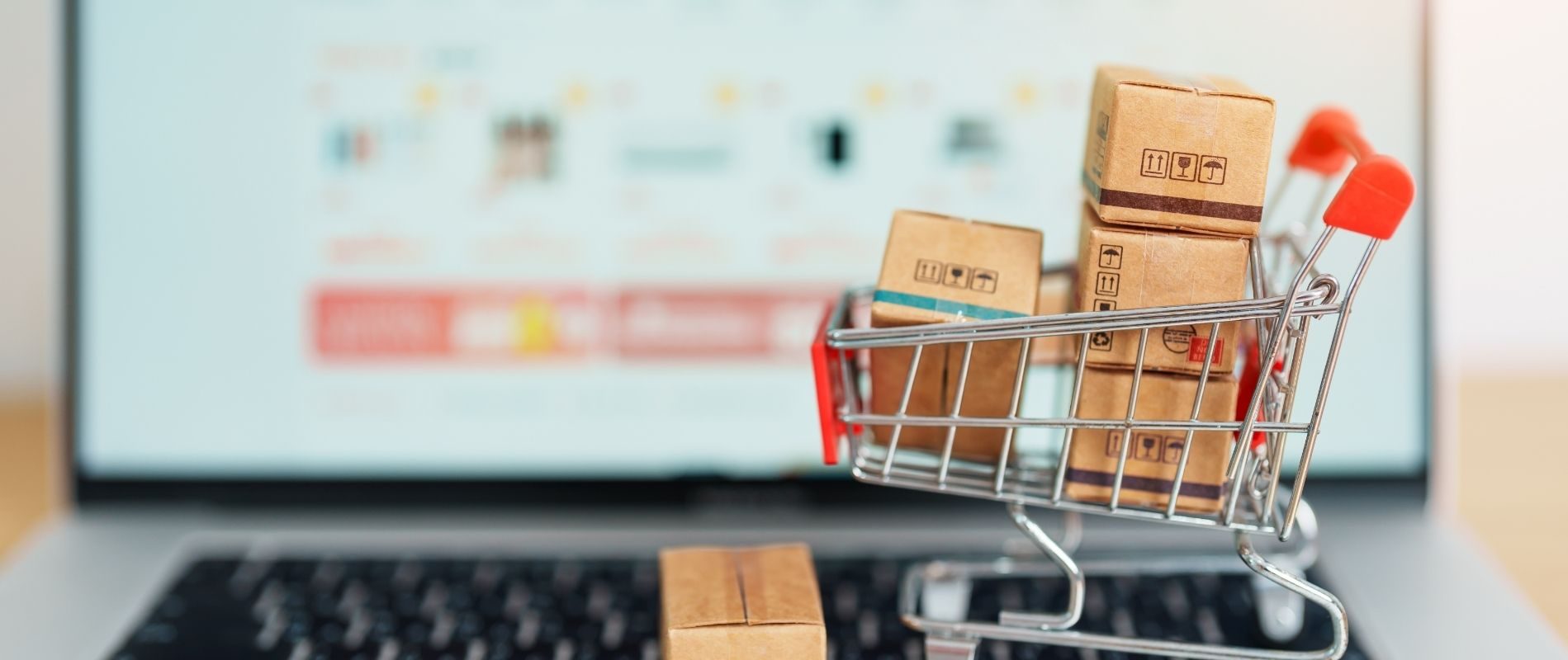 Mini shopping cart with cardboard boxes on laptop keyboard, representing online shopping and e-commerce logistics.