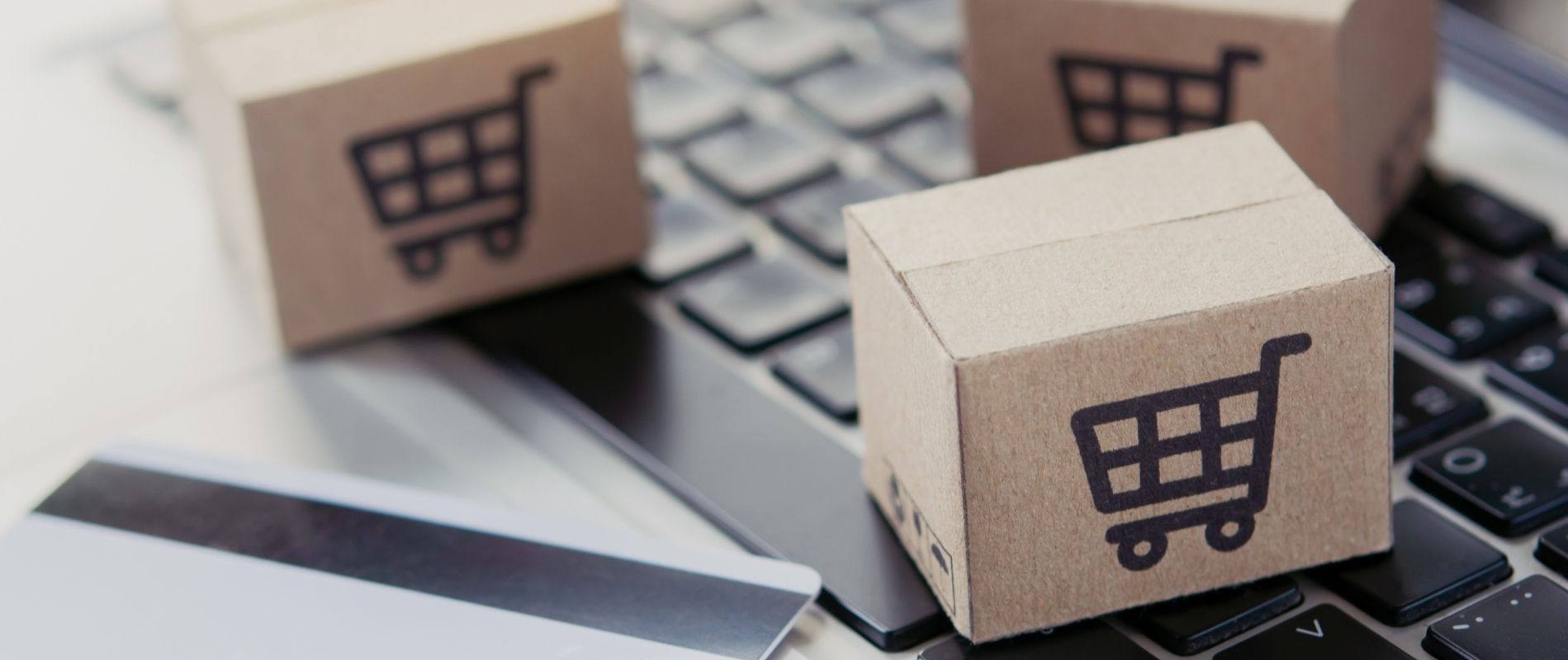 Small shipping boxes with shopping cart icons on a laptop keyboard, depicting e-commerce and online shopping concepts.