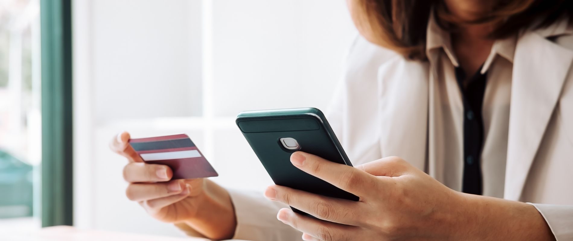 Person making an online payment using a smartphone and credit card, close-up on hands. Online shopping concept.