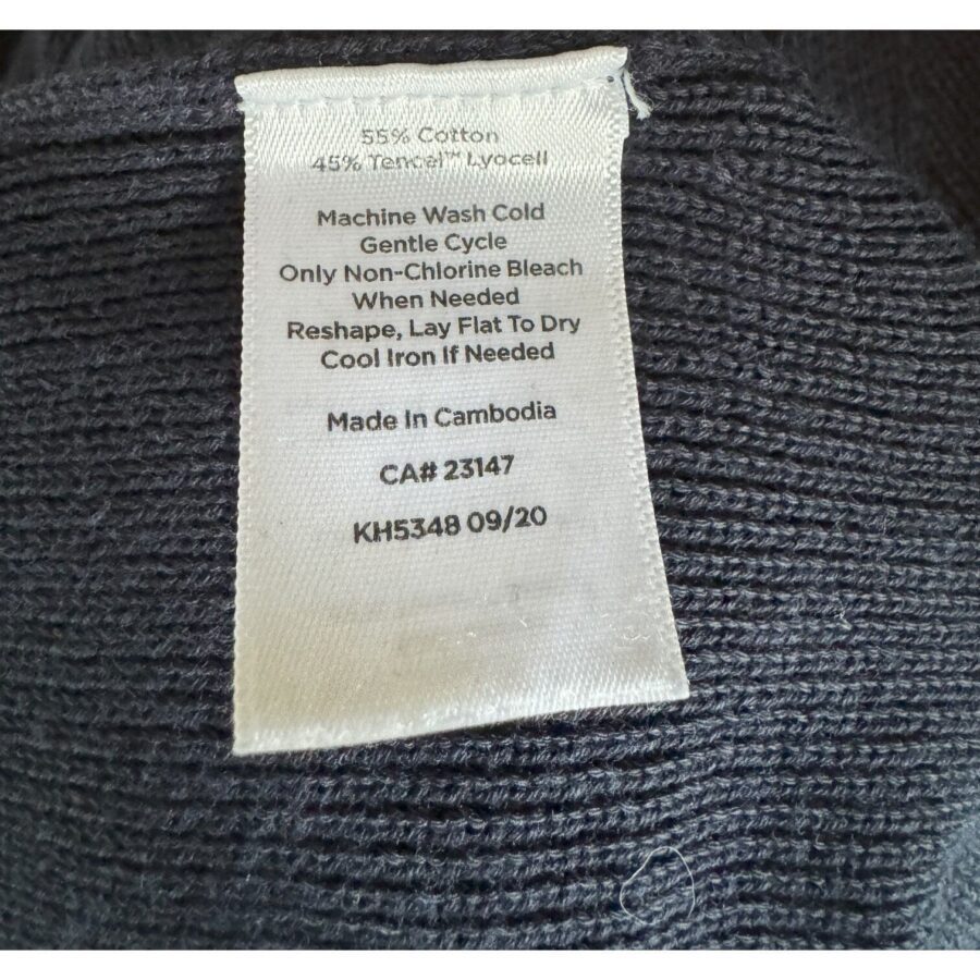 A close-up of a clothing care label detailing fabric composition, washing instructions, and manufacturing location on a dark-colored knitted fabric.