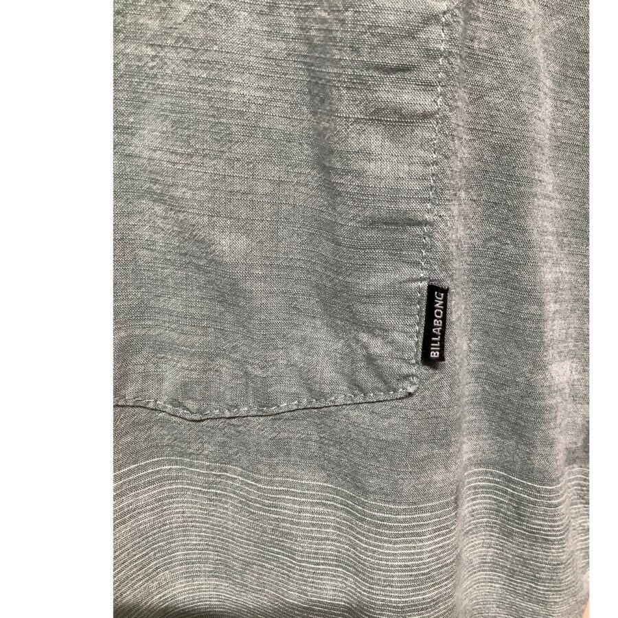 Close-up image of a gray fabric with visible texture and pocket stitching, featuring a small label with the text "BILLABONG." No landmarks or historical buildings present.