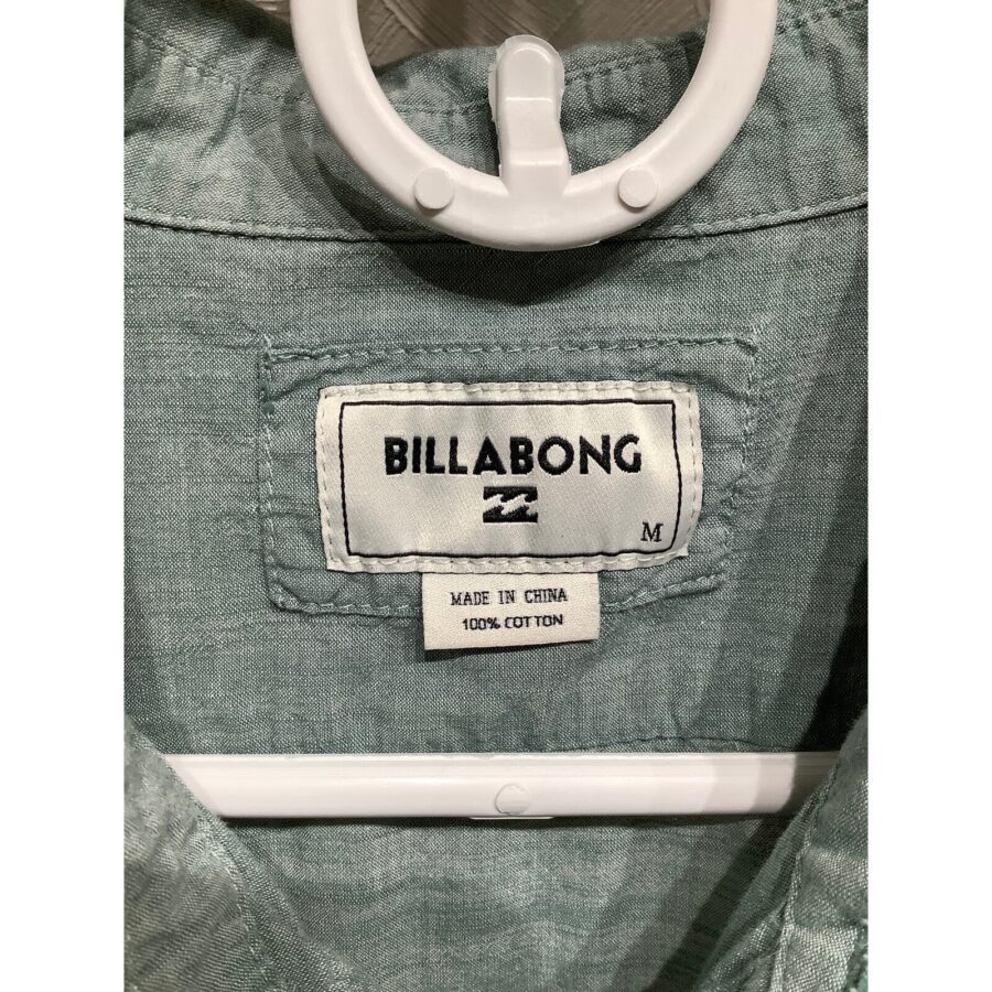 A Billabong shirt with a clothing tag, hanging on a white hanger. The tag indicates it is made in China and 100% cotton.