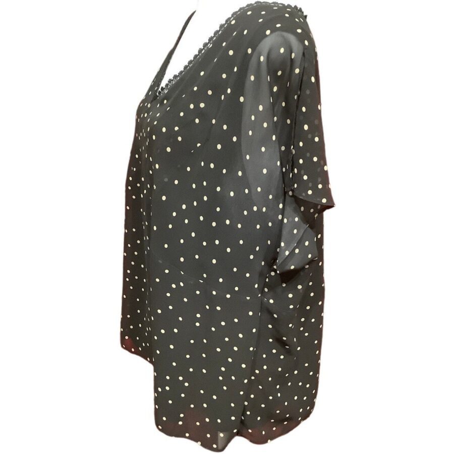 A black, loose-fitting blouse with white polka dots, featuring short sleeves and a V-neck design, displayed on a mannequin torso.