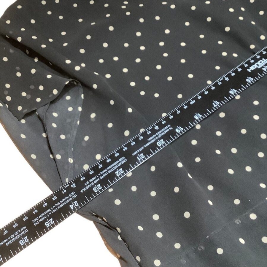 A dark fabric with white polka dots is shown, with a ruler placed diagonally across it, measuring its length. No landmarks or historical buildings appear.