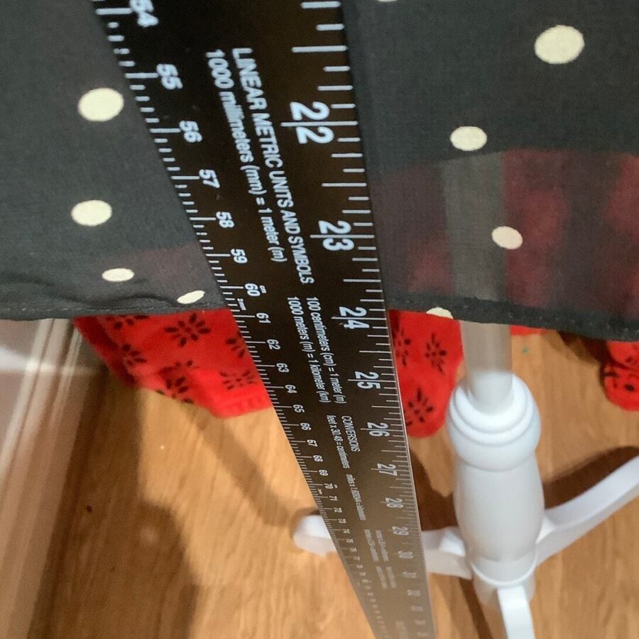 A black ruler measuring fabric with polka dots, red patterned material underneath, white stand on wooden floor inside a room with no landmarks visible.