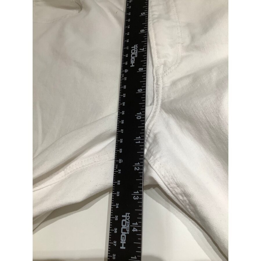 A black ruler measuring a white garment laid flat on a surface. The ruler's markings are in inches and centimeters, indicating precise measurements.