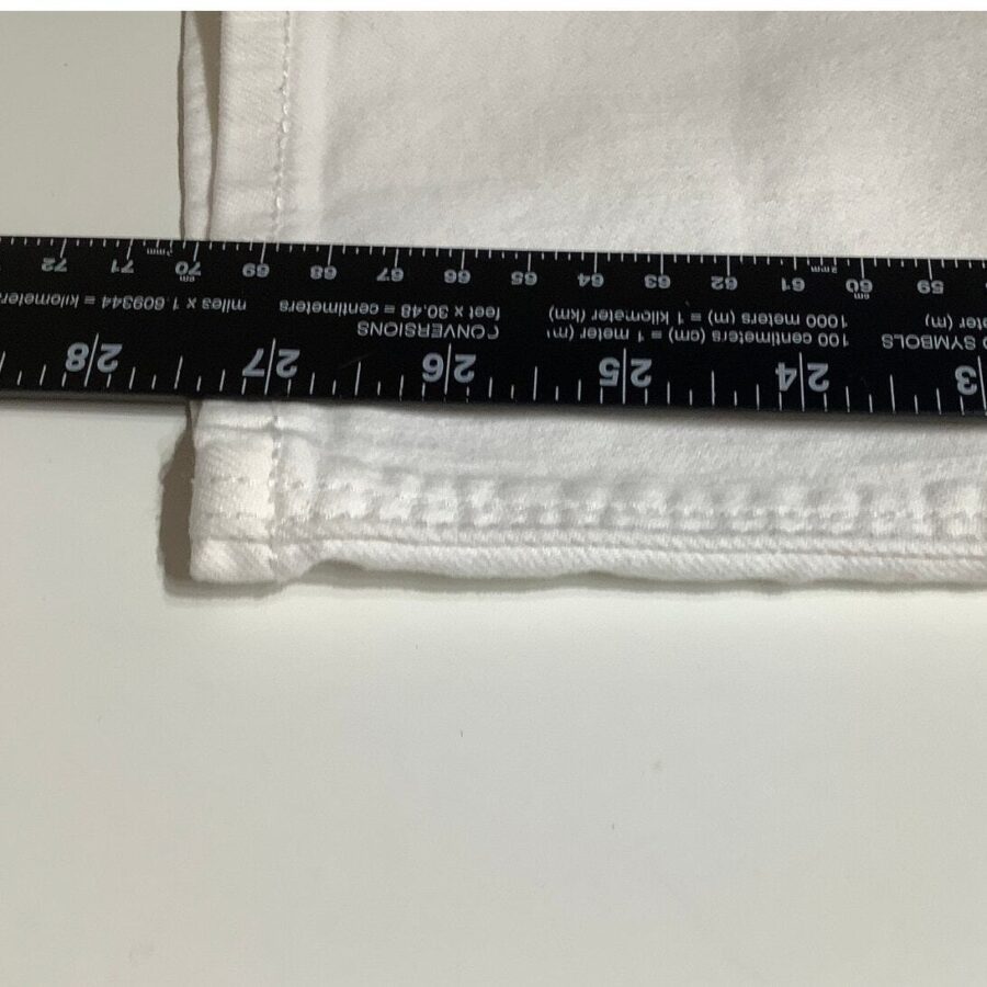 A close-up image of a black ruler measuring the width of a folded white fabric against a white background, showing precise inches and millimeters.