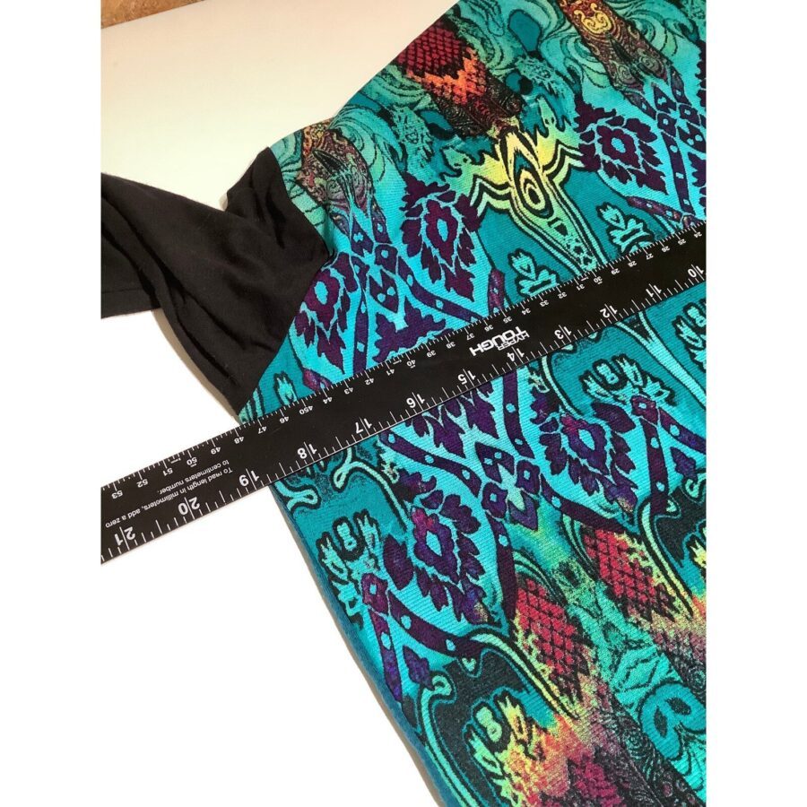 A colorful fabric with a vibrant pattern is being measured with a black 12-inch ruler, featuring intricate designs in turquoise, purple, and red hues.