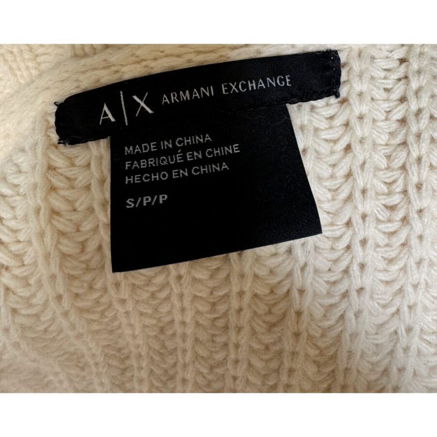 A close-up of an Armani Exchange clothing tag on a thick, cream-colored knit fabric, indicating it's made in China and size S/P/P.