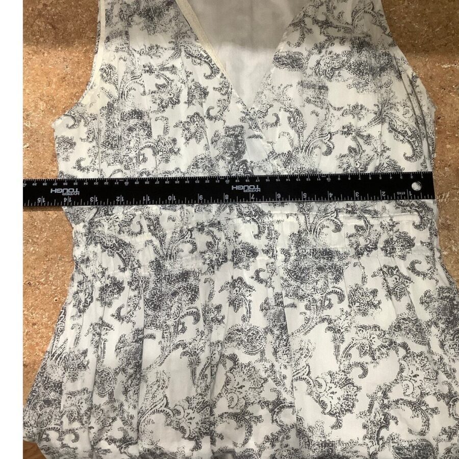 A ruler measures the width of a sleeveless, patterned blouse with a floral design, laid out on a textured surface.