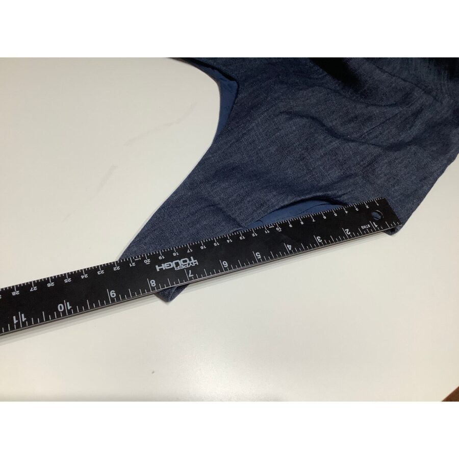 A black ruler measuring a blue fabric placed on a white surface. The ruler has both metric (centimeters) and imperial (inches) units.