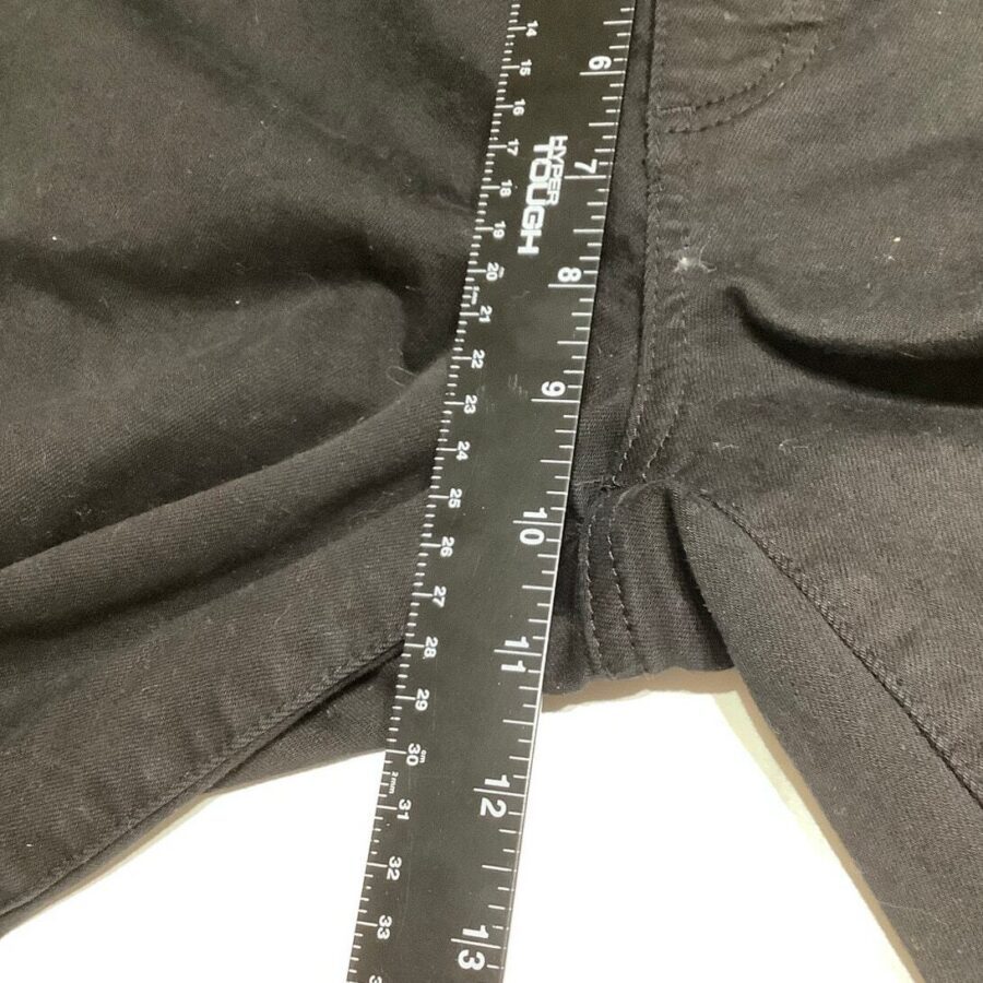 Black pants are measured with a black, 36-inch ruler placed across the waistband. Measurement indicates approximately 20 inches. The background is white.