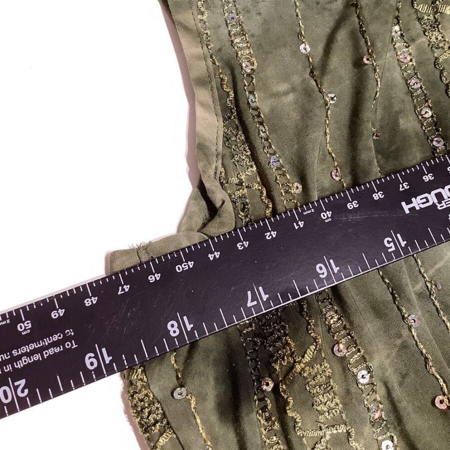 A black ruler measures green, sequined fabric against a white background. The ruler's markings are shown in both inches and centimeters.