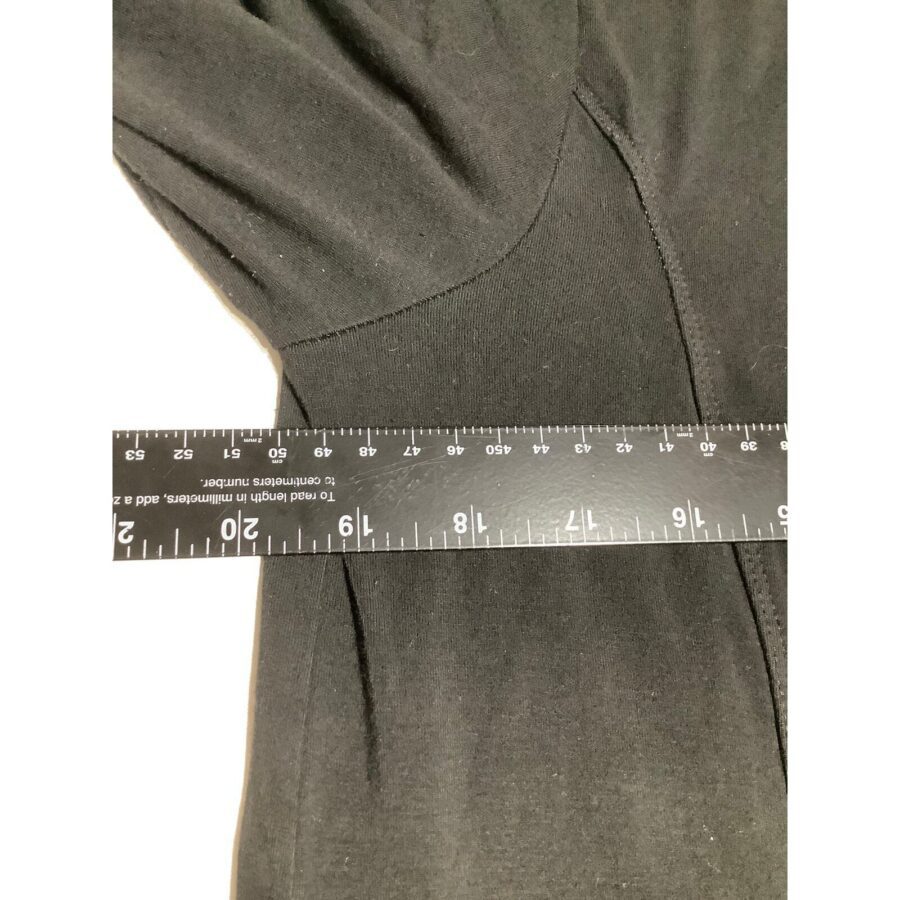 A black garment is being measured by a ruler, indicating dimensions in inches and centimeters. The fabric features some visible seams and stitching.