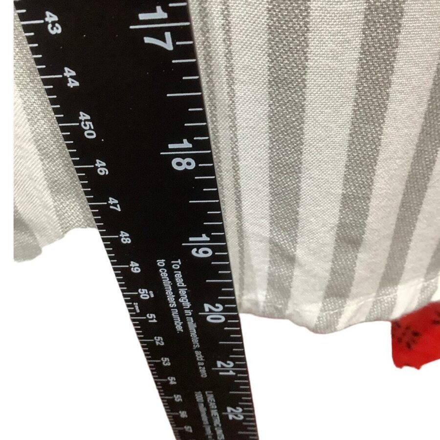 Close-up of a black measuring ruler next to a light gray and white striped fabric. The ruler shows measurements in inches and centimeters.