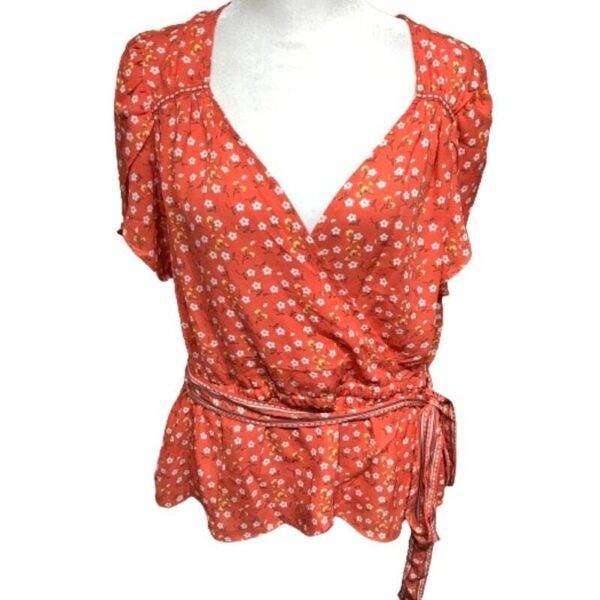 The image shows an orange floral wrap blouse with short sleeves and a waist tie on a white garment stand against a plain background.