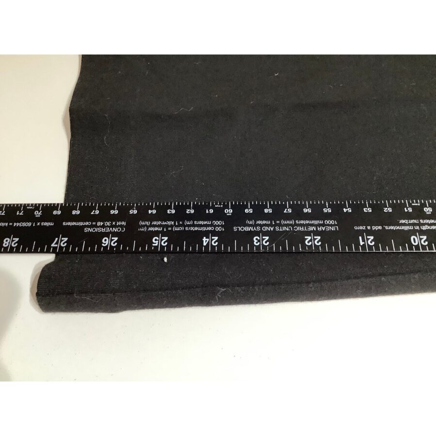 A black fabric is placed on a flat surface with a black ruler measuring its length, showing measurements up to 24 inches.