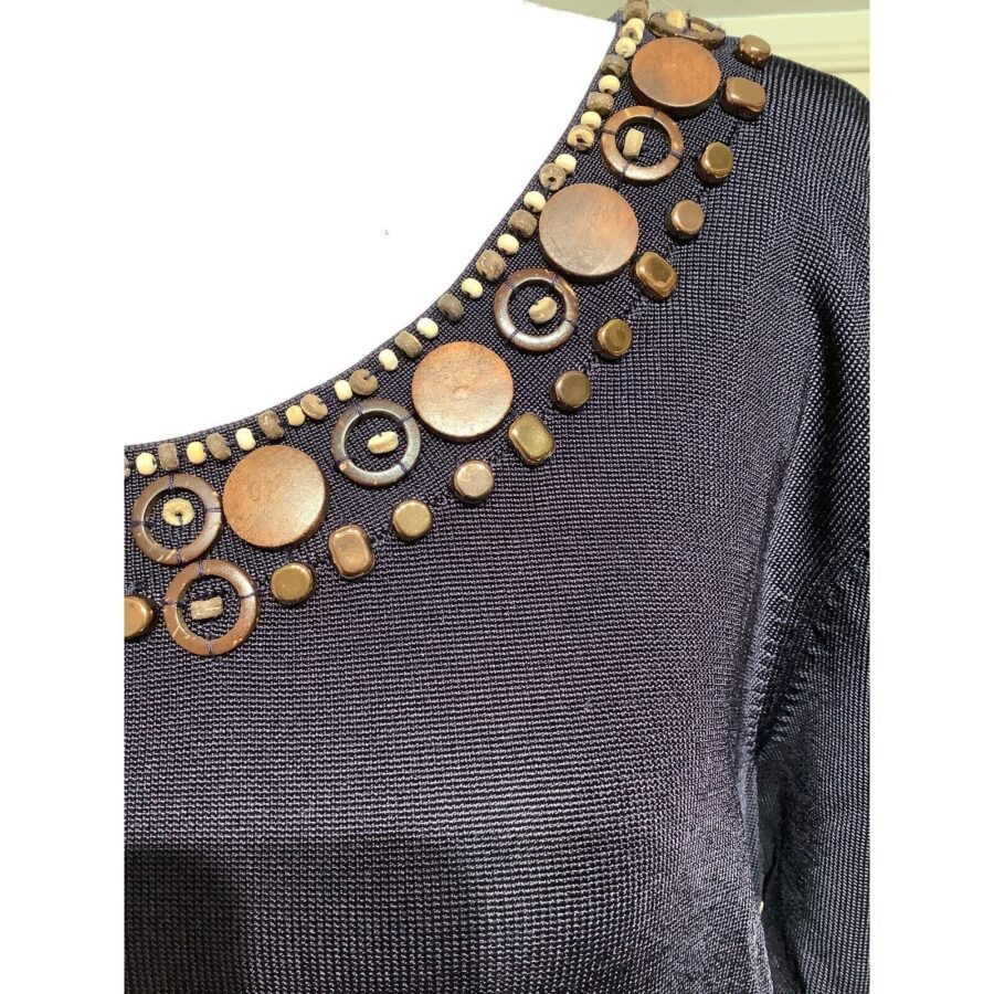 Close-up of a black fabric top adorned with round and square gold-colored decorative elements around the neckline. No landmarks or historical buildings visible.