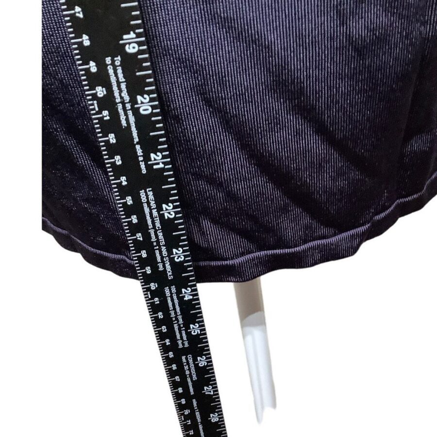 A ruler measuring the length of a black fabric, placed near a white stand. The fabric appears to have a fine vertical stripe pattern.