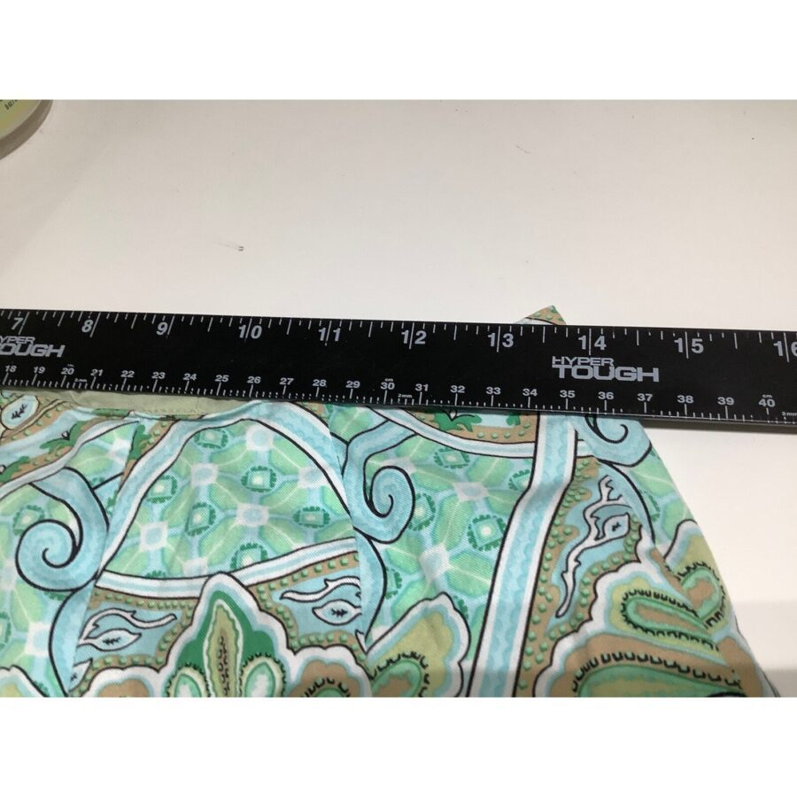 A ruler measuring a patterned green and blue fabric with intricate designs, placed on a white surface. No landmarks or historical buildings are visible.