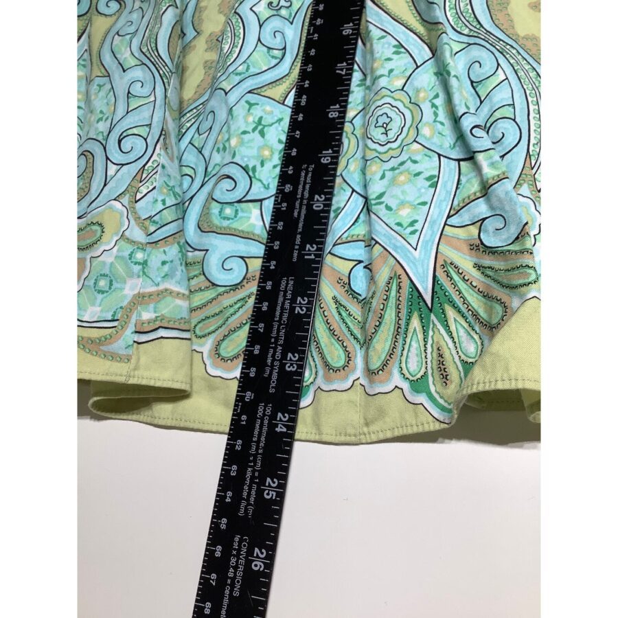 A ruler measures a colorful, intricately patterned fabric with green, blue, and yellow designs on a white background. No landmarks or historical buildings.