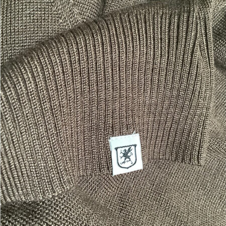 A close-up of a textured brown sweater with a small white label featuring a black coat of arms-like design, folded neatly.