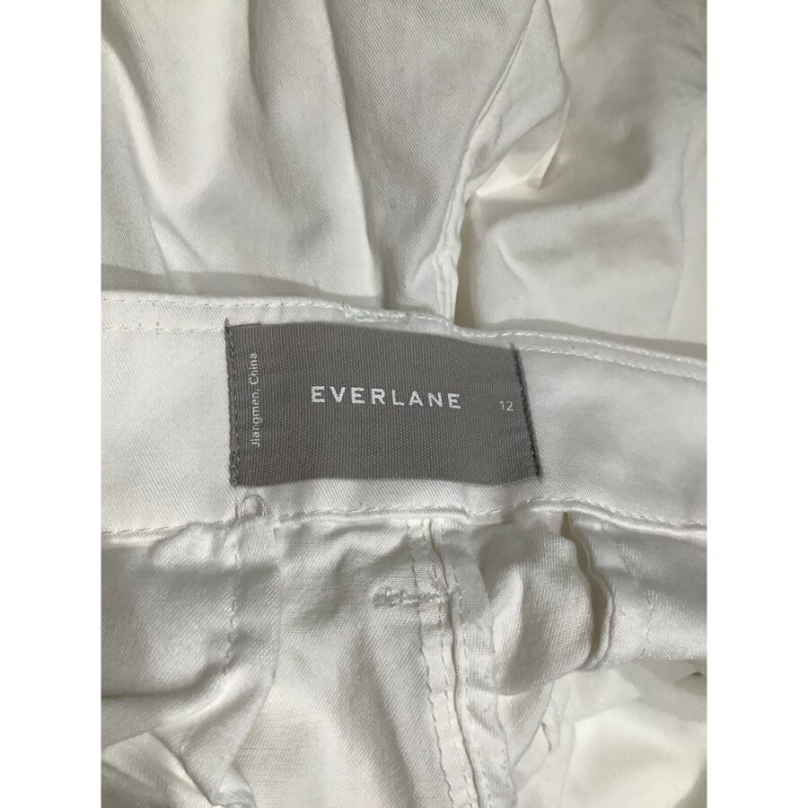 Close-up image of a white garment's inner tag, displaying the brand "EVERLANE" and size "12" on a gray background.