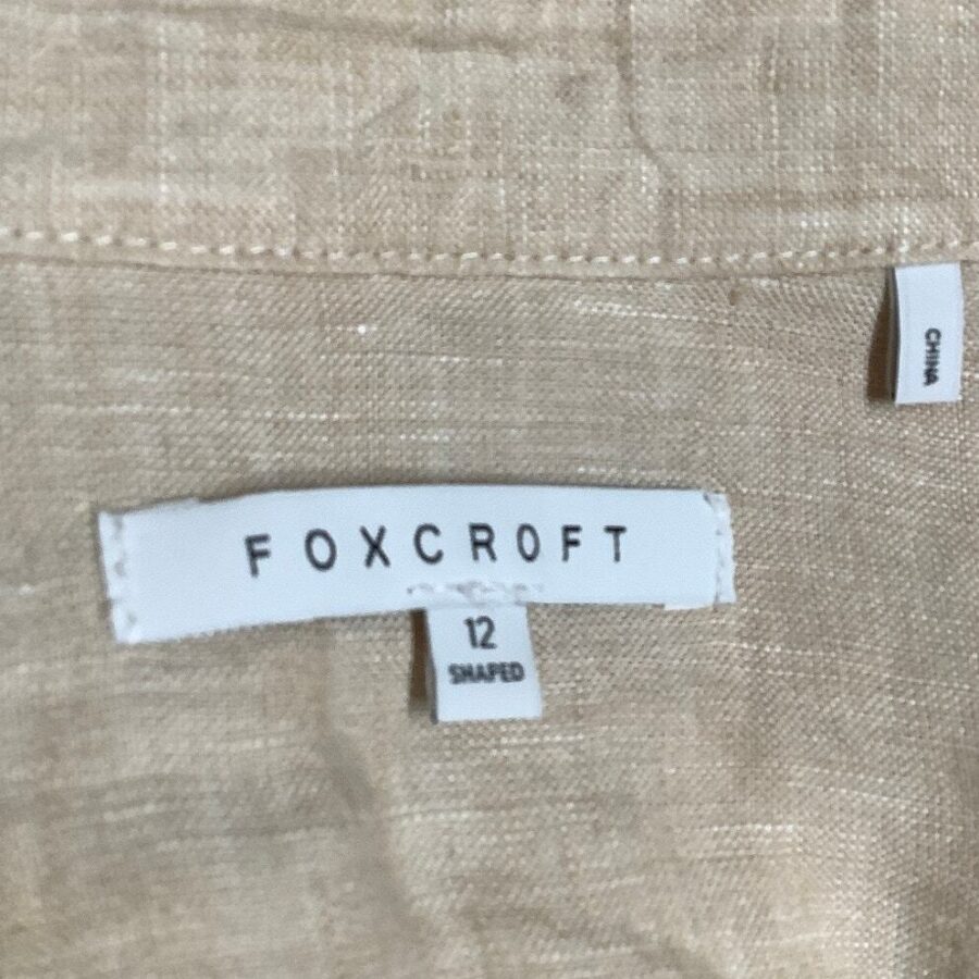 A close-up of a clothing label reading "FOXCROFT," size 12. Fabric is beige; an additional label indicates the item was made in China.