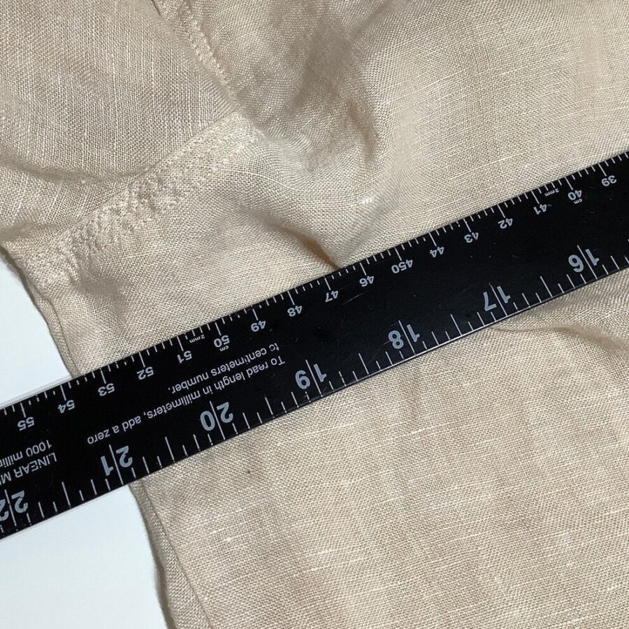 A black measuring ruler is placed over a piece of light beige fabric, showing measurements in both centimeters and inches.