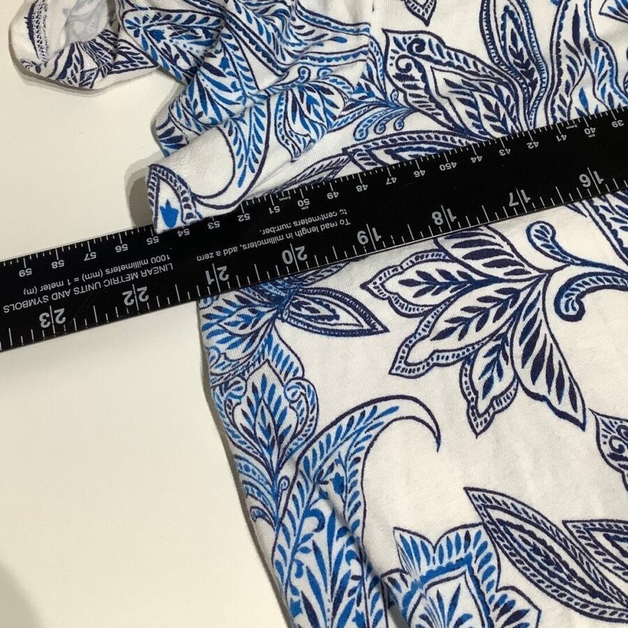 A ruler is placed on fabric with a blue floral pattern, displaying measurements in inches and centimeters. The background is plain and off-white.