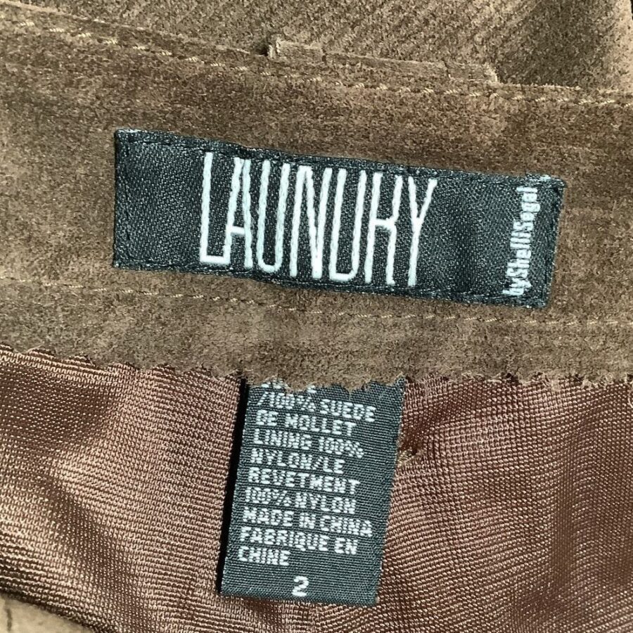 A close-up image of two clothing labels showing brand name "Laundry" by Shelli Segal, material composition, and care information on brown fabric.