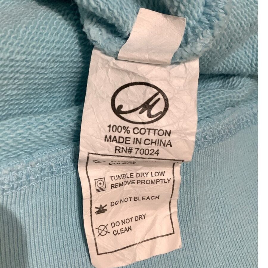 This image shows a clothing label on a blue fabric, indicating it is 100% cotton, made in China, with care instructions for drying and cleaning.