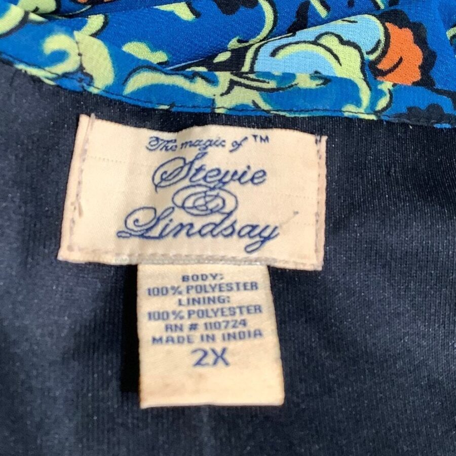 A clothing label reads "The magic of Stevie Lindsay." The fabric is 100% polyester and made in India, size 2X. The clothing features colorful patterns.