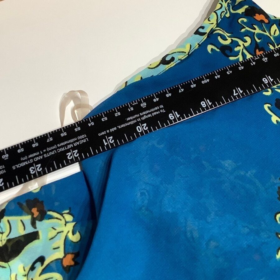 A close-up view of a fabric with floral patterns, measured with a black ruler indicating inches and centimeters. No landmarks or historical buildings visible.