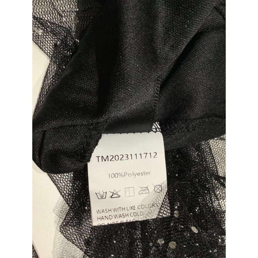 A close-up of a black polyester garment with a care label displaying wash instructions and material information. No recognizable landmarks or historical buildings present.