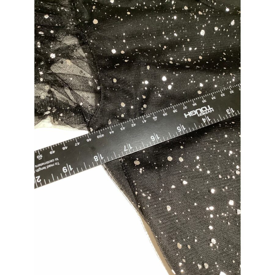 A close-up image of black fabric with white speckles and a ruler measuring it. The fabric lies flat on a white surface.